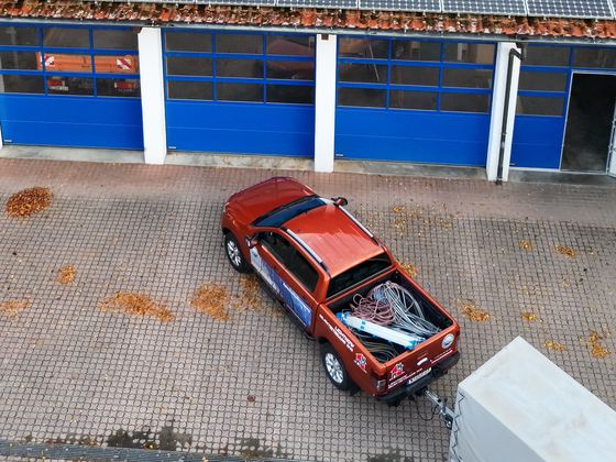 Gepflasterter Hof vor Hallentoren mit Pick-up und Anhänger, Laub auf dem Pflaster, von oben aufgenommen
