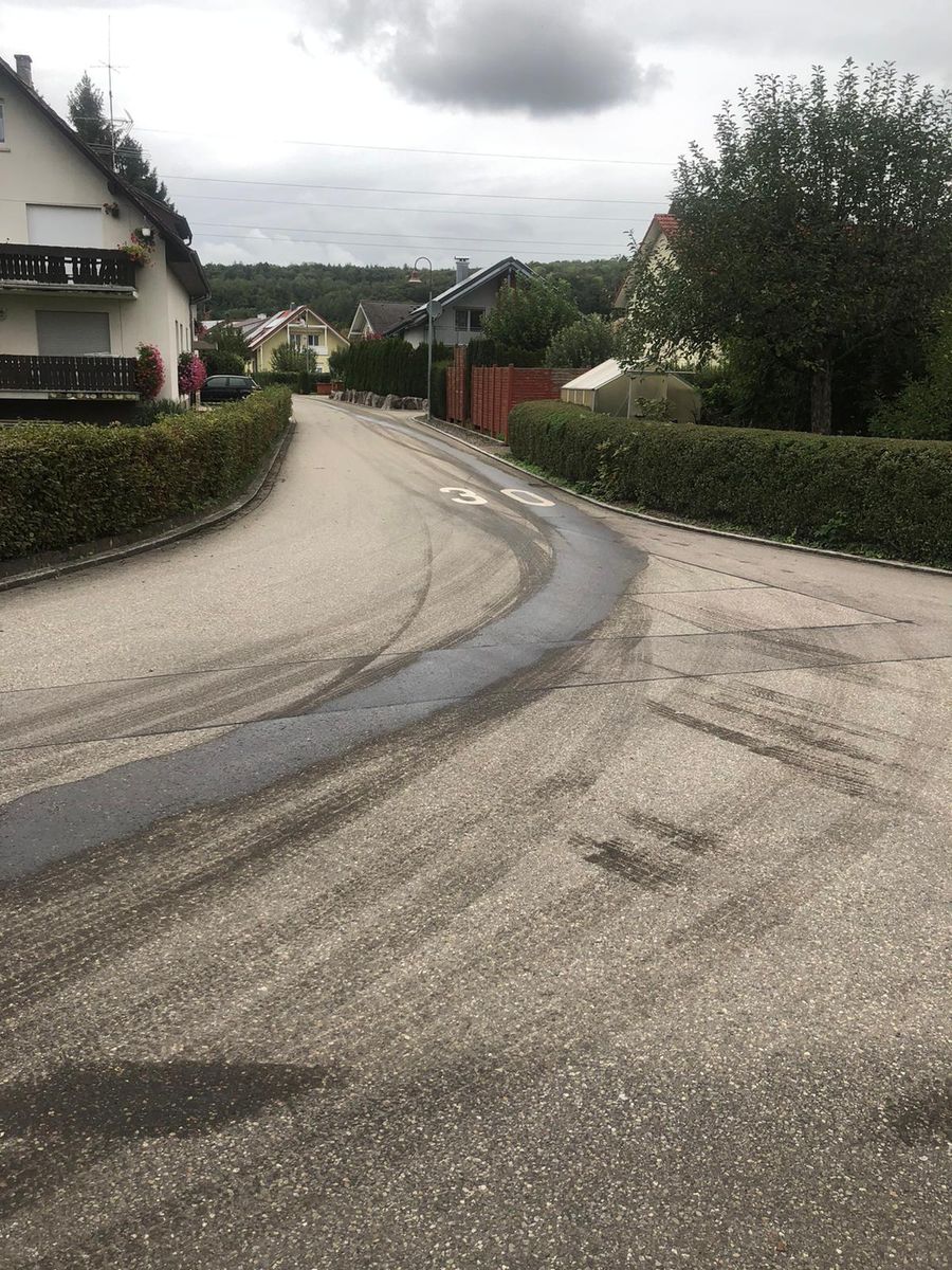 Ölspur als dunkle Spur in einer Kurve einer Ortsstraße
