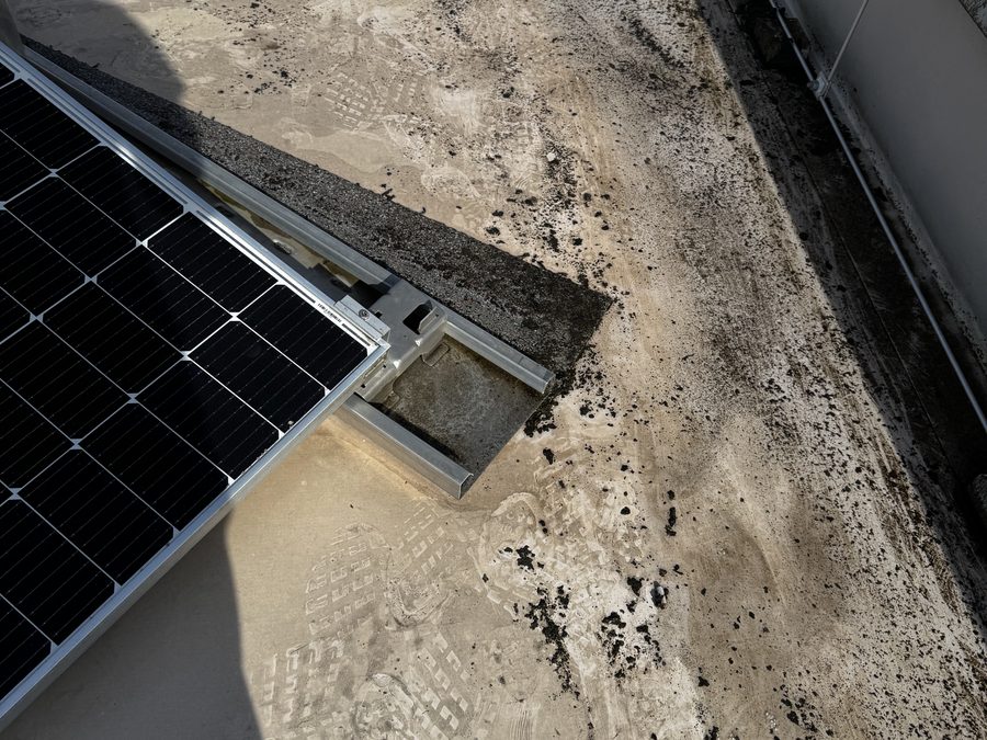 Schmutz und dunkle Ablagerungen auf der Dachfläche neben dem Fuß eines Solarmoduls und am Dachrand