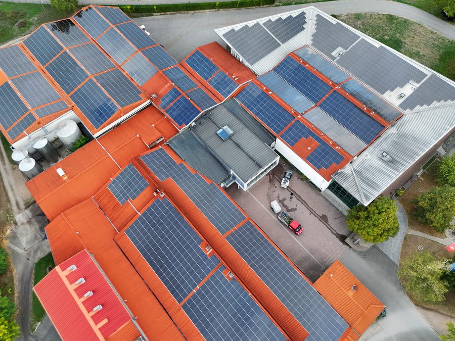 Photovoltaikanlagen auf mehreren Hallendächern mit orangen Dachflächen, senkrecht von oben aufgenommen