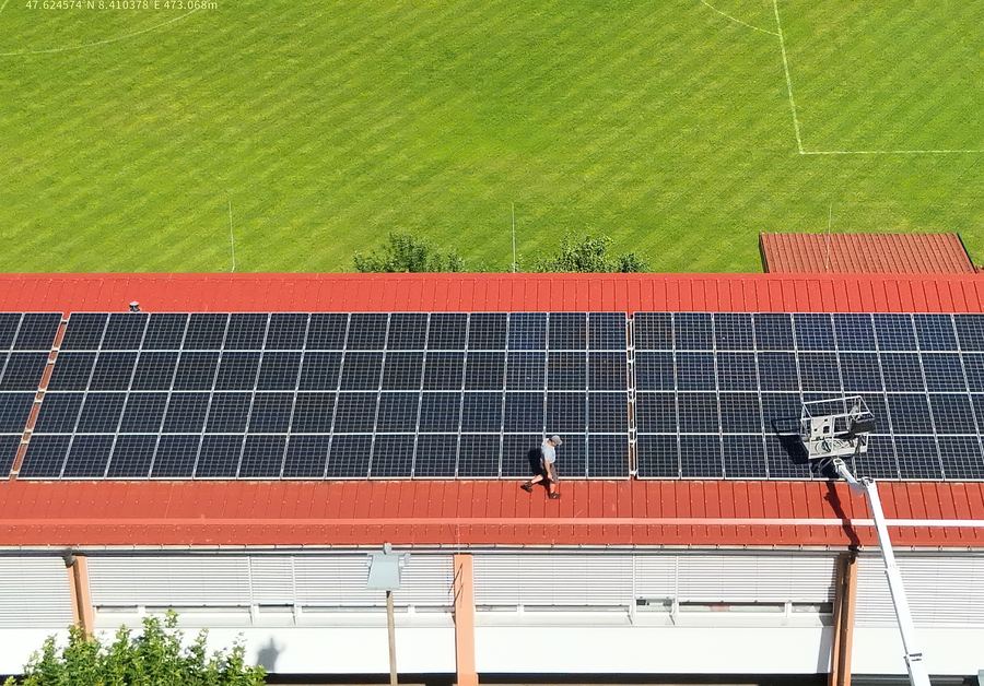Arbeiter auf einem Hallendach mit Photovoltaikanlage, daneben ein Hubsteiger