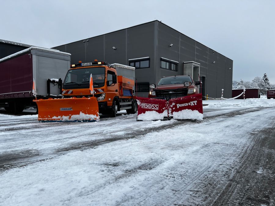 Zwei Räumfahrzeuge mit Schneeschild vor einer Gewerbehalle